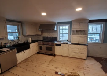 Off-white kitchen cabinets with some installation damage, black countertops, stainless steel appliances, and unfinished wood floor in Amherst NH