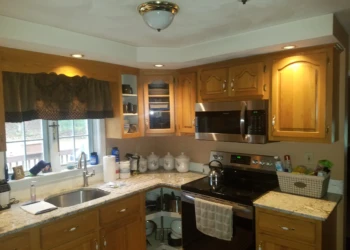 Kitchen with wooden cabinets, granite countertops, stainless steel stove and microwave before cabinet refinishing in Pelham, NH