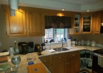 Wooden kitchen cabinets with a natural finish around a sink beneath a window in Pelham, NH kitchen