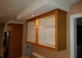 Empty wooden kitchen cabinets mounted on wall above granite countertop during refinishing preparation in Pelham, NH kitchen
