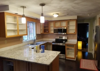 Kitchen with wooden cabinets stripped and prepared for refinishing, granite countertops and stainless steel appliances in Pelham, NH kitchen