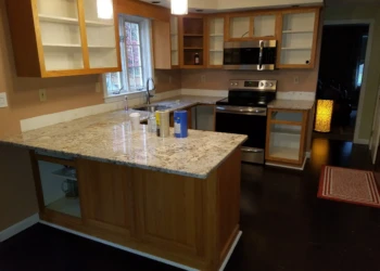 Wood kitchen cabinets in Pelham NH partially empty with granite countertops and stainless steel appliances during cabinet refinishing preparation