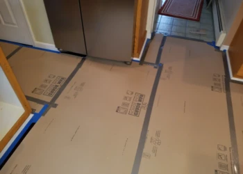 Floor protection with cardboard and tape in a kitchen before cabinet refinishing in Pelham, NH