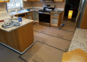 Kitchen with cabinets prepped for cabinet refinishing in Pelham NH, floor protected with cardboard sheets and blue painter's tape