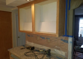 Open wood kitchen cabinets with tools on granite countertop indicating cabinet refinishing in Pelham NH