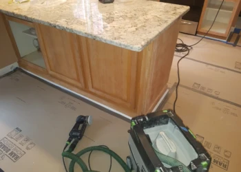 Wooden kitchen island cabinet with protective floor covering and power sanding tool during cabinet refinishing in Pelham NH