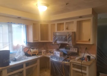 Primed kitchen cabinets in the process of cabinet refinishing in Pelham, NH with protective plastic covering appliances
