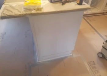 Close-up of freshly refinished kitchen cabinet base with protective covering on countertop in Pelham, NH