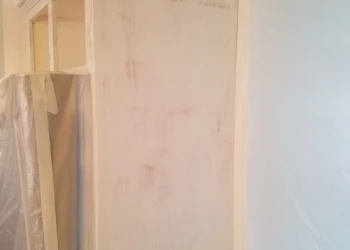 Close-up of a kitchen cabinet during the finishing stage in a Pelham NH home showing a partially coated cabinet surface