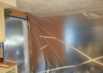 Plastic sheeting taped over kitchen walls and cabinets to protect areas during cabinet refinishing work in Pelham NH