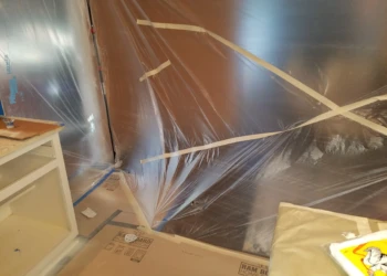 Plastic sheeting taped over kitchen walls and floors for cabinet refinishing protection in Pelham, NH