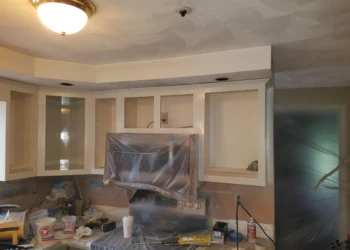 Upper kitchen cabinets partially refinished and masked for protection during cabinet refinishing in Pelham NH