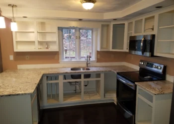 Kitchen with freshly refinished white cabinets and granite countertops around stainless steel stove and sink under window in Pelham, NH