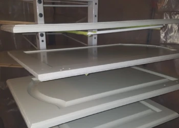 Several kitchen cabinet doors primed and hanging on racks during cabinet refinishing in Pelham NH