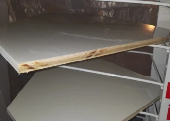 Close-up of kitchen cabinet shelves primed and drying on white metal rack during cabinet refinishing in Pelham NH