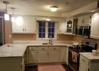 Refinished cream kitchen cabinets surrounding granite countertops and stainless steel appliances in a Pelham, NH kitchen