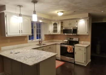 Light-colored refined kitchen cabinets with granite countertops, stainless steel appliances, and pendant lighting in Pelham, NH kitchen