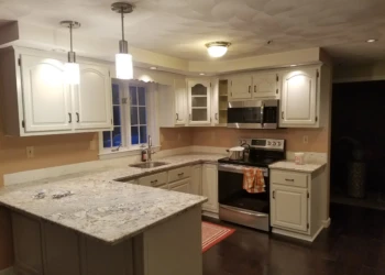 Kitchen with cream-colored refinished cabinets and granite countertops around stainless steel appliances in Pelham NH