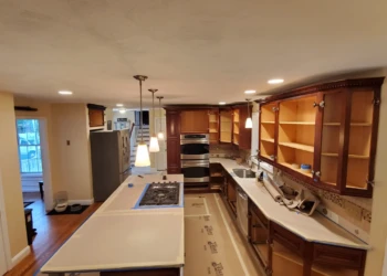 Mid-renovation kitchen with upper and lower wooden cabinets, countertops covered and doors removed in Windham, NH