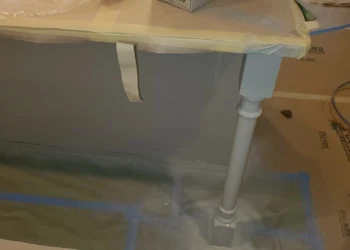 Close-up of a painted kitchen cabinet leg and corner, floor protected with cardboard and plastic during cabinet painting in Windham, NH
