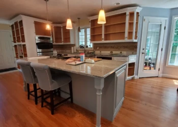 Kitchen with bare wooden cabinets and gray painted island in a home in Windham, NH ready for cabinet painting