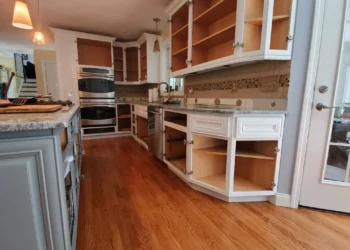 Open kitchen cabinets and drawers with white painted finish in a kitchen with hardwood floors and granite countertops